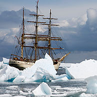 The tallship Europa, a three-masted barque seen through gap in iceberg, Port Charcot, Antarctica