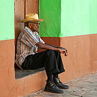 Portrait of old Cuban man sitting in front of pastel coloured house front in the streets of Trinidad, Cuba