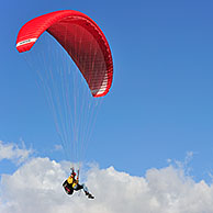 Paraglider in flight with red wing / canopy against blue cloudy sky, Brittany, France