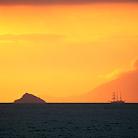 Sailing ship at sunset in front of the island Santiago, Galapagos