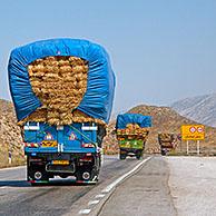 Convoy of heavily loaded trucks transporting bales of hay over highway in Iran